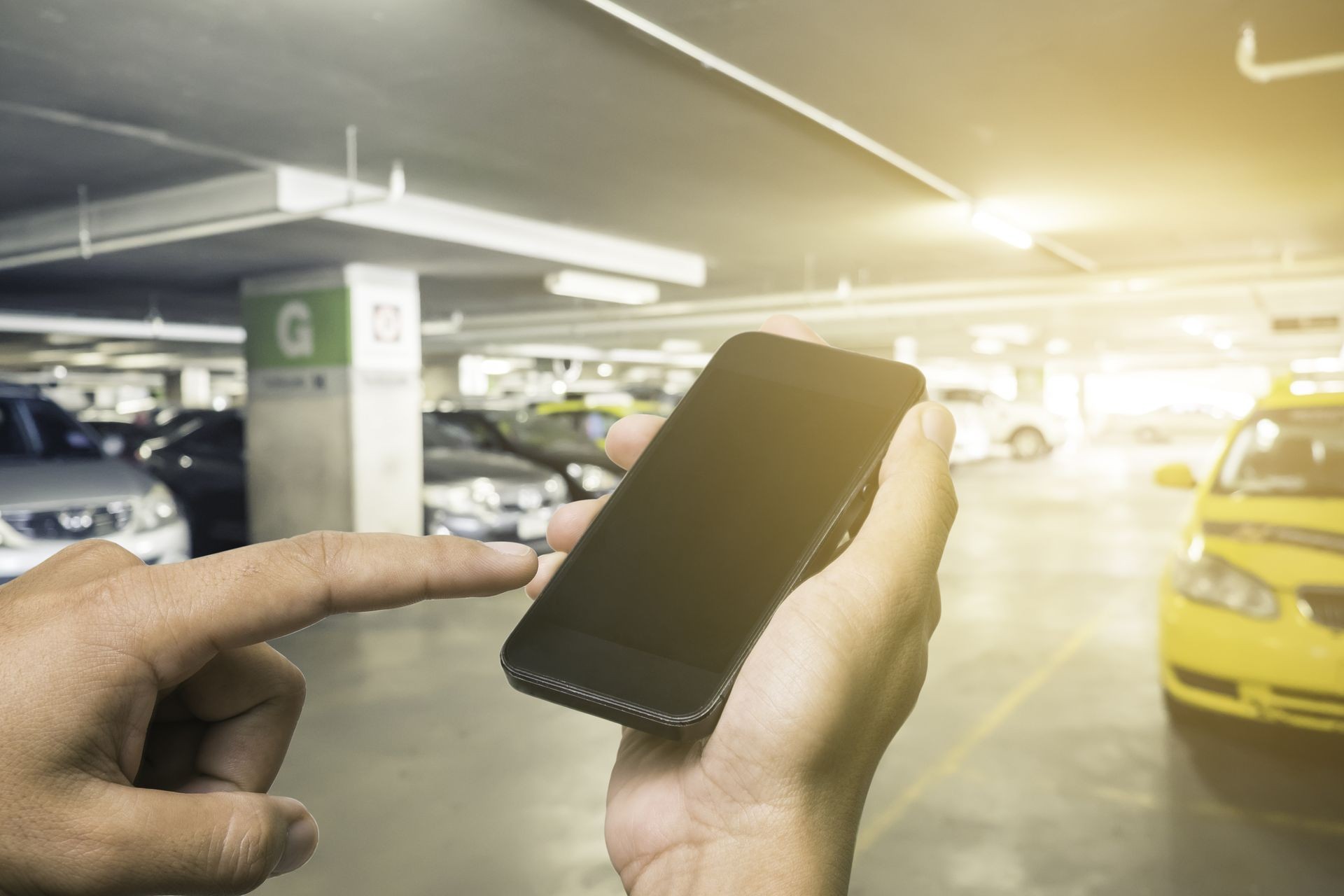 hands holding mobile phone with blur cars parking.Hand of a man holding a smartphone and touching the screen.Parking lot